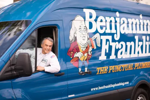 Benjamin Franklin Plumbing Tech, Jose, smiling as he looks out his van's window in front of a Orlando FL home