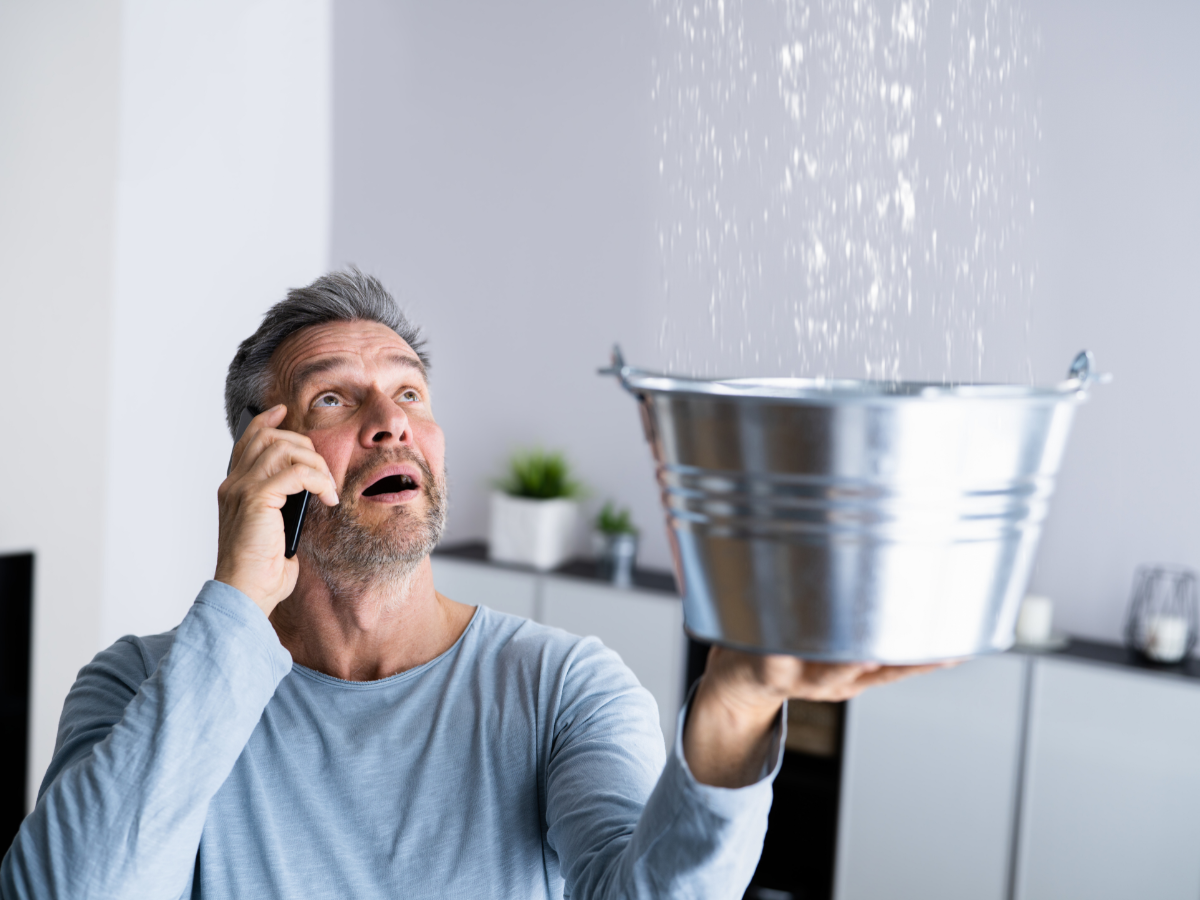 Man using to bucket to catch leaking water during plumbing emergency
