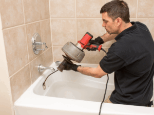 professional plumber using auger method to clear slow draining tub